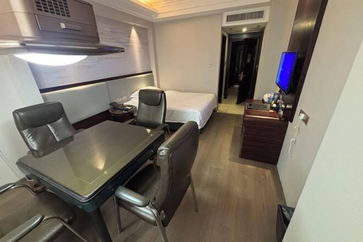 Ein kleines Hotelzimmer mit Esstisch, zwei Stühlen, einem Bett, einem Fernseher und einer kleinen Küchenzeile.