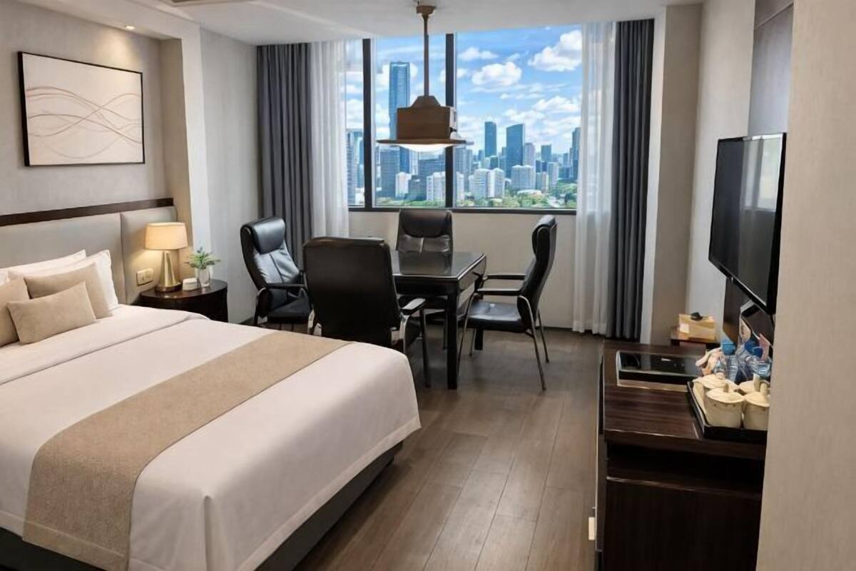 Ein Hotelzimmer mit Bett, Schreibtisch, Stühlen, Fernseher und Blick auf die Stadt.
