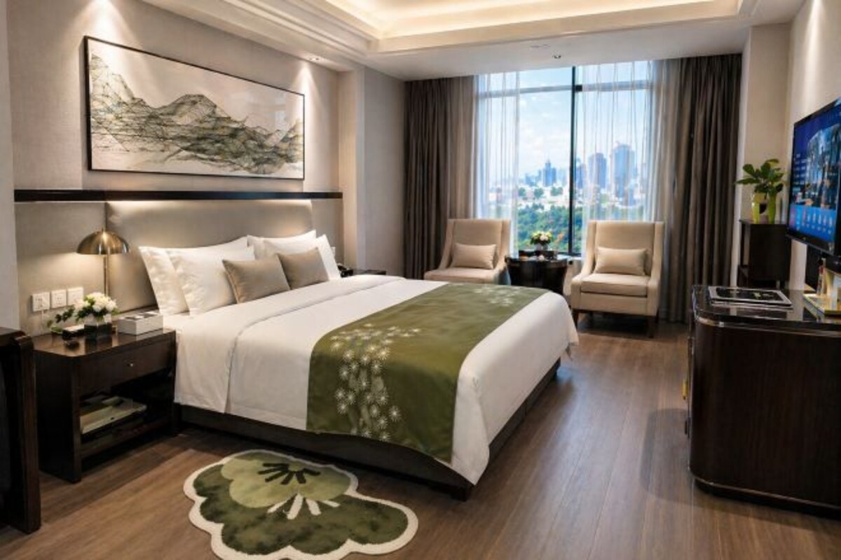 Habitación de hotel con cama, dos sillones, un escritorio, televisor y un ventanal con vistas a la ciudad.