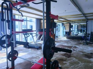 Ein Fitnessraum mit Trainingsgeräten, Laufband und einer roten Hantelbank.