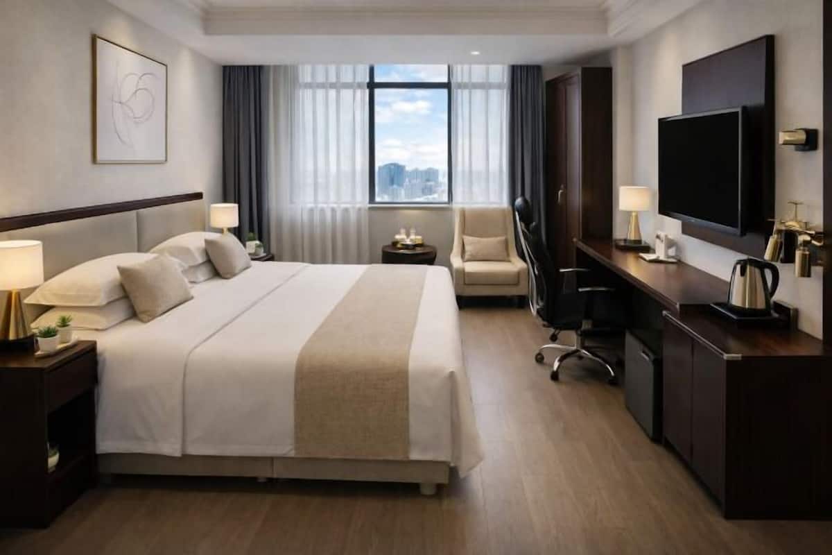 Ein Hotelzimmer mit einem großen Bett, einem Schreibtisch mit Fernseher, einem Sessel, einem Nachttisch und einem Fenster mit Blick auf die Stadt.