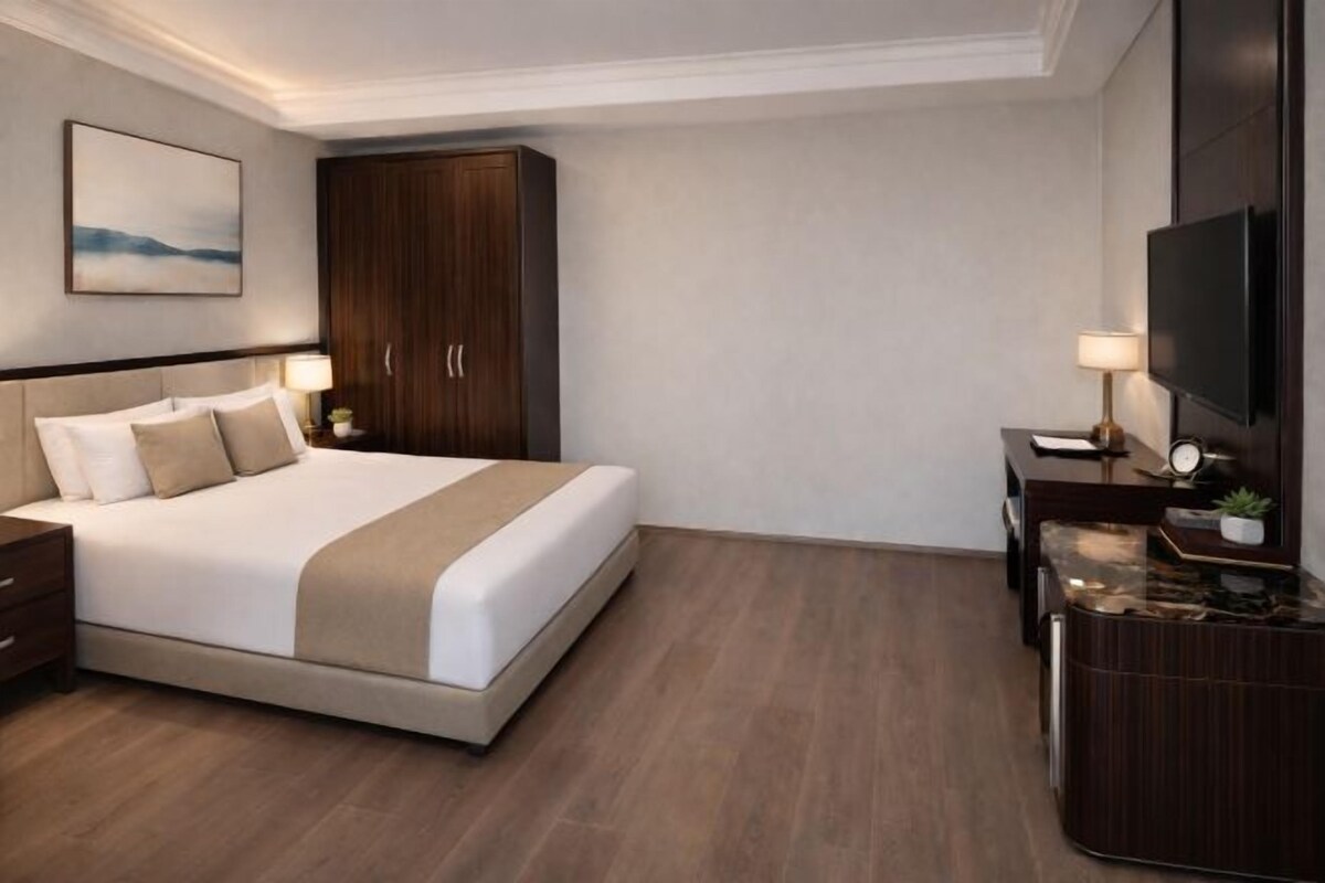 Habitación de hotel con una cama, un armario, un escritorio con lámpara y un televisor.