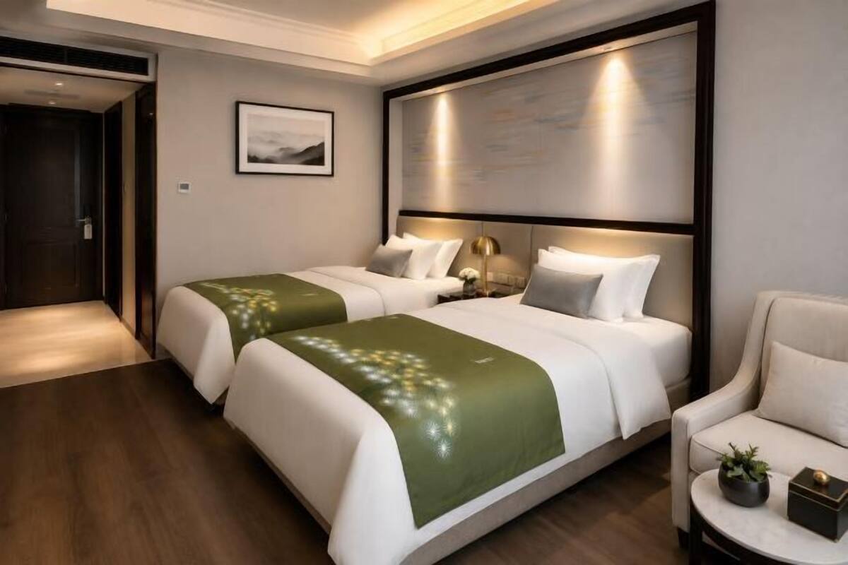 Ein Hotelzimmer mit zwei Betten, einem großen Wandbild, einem gerahmten Bild, einem kleinen runden Tisch mit Pflanze und einem Sessel.
