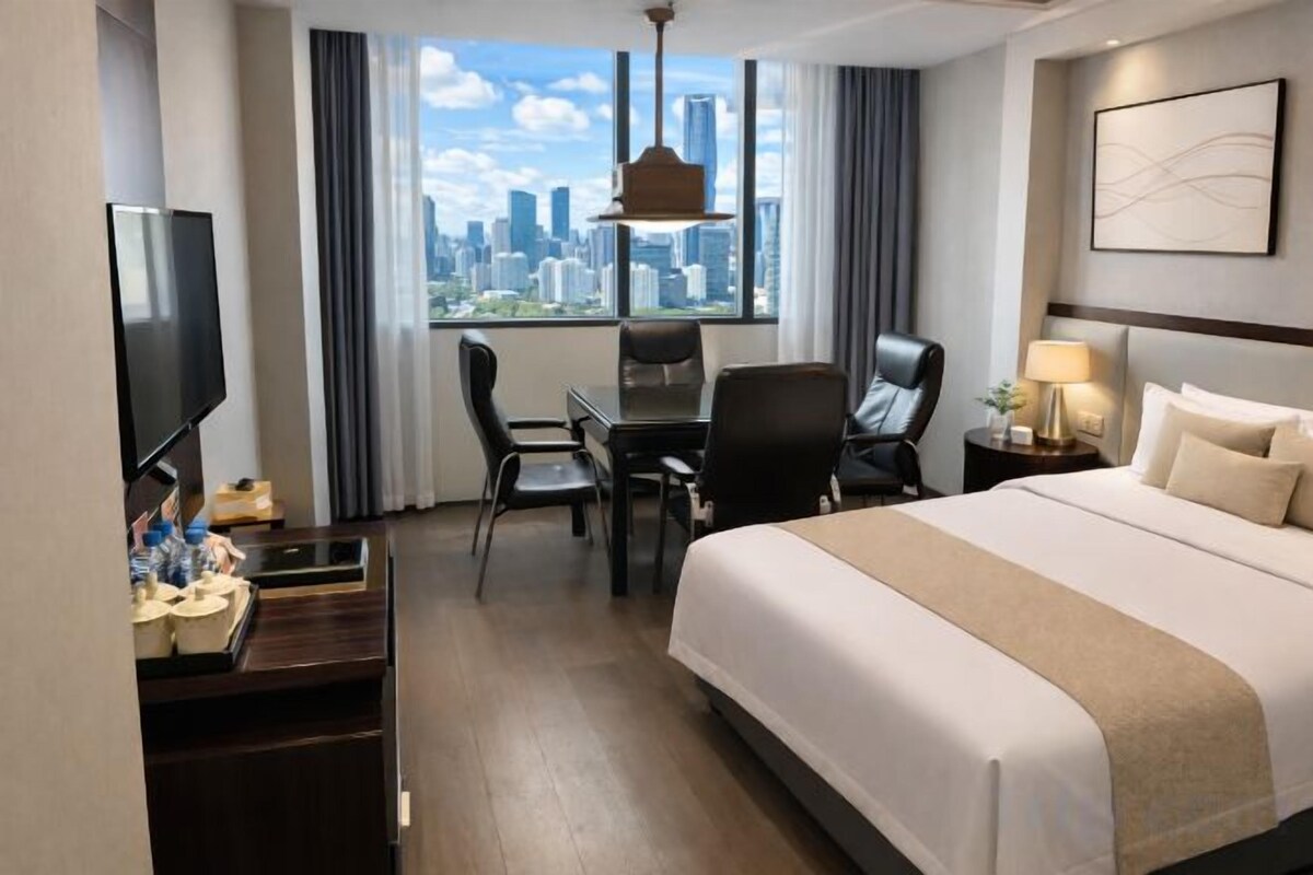 A hotel room with a bed, a desk, a chair, a TV, and a window with a city view.