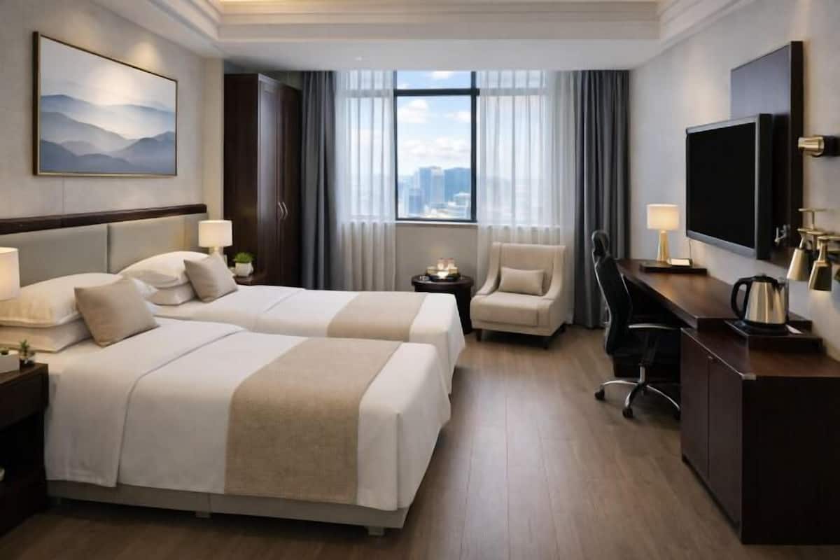 Ein Hotelzimmer mit zwei Betten, einem Schreibtisch, einem Sessel, einem Fernseher und einem Fenster mit Blick auf die Stadt.