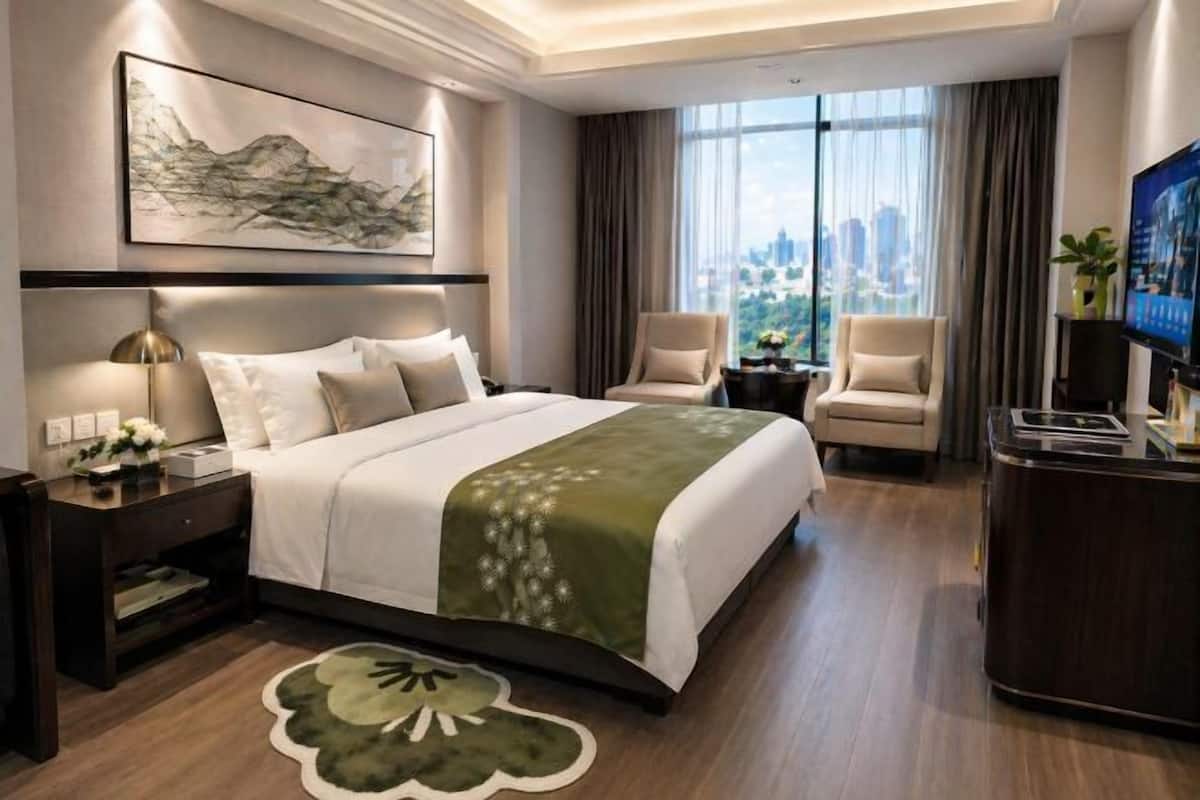 Ein Hotelzimmer mit einem Bett, zwei Sessel, einem Schreibtisch, einem Fernseher und einem großen Fenster mit Blick auf die Stadt.