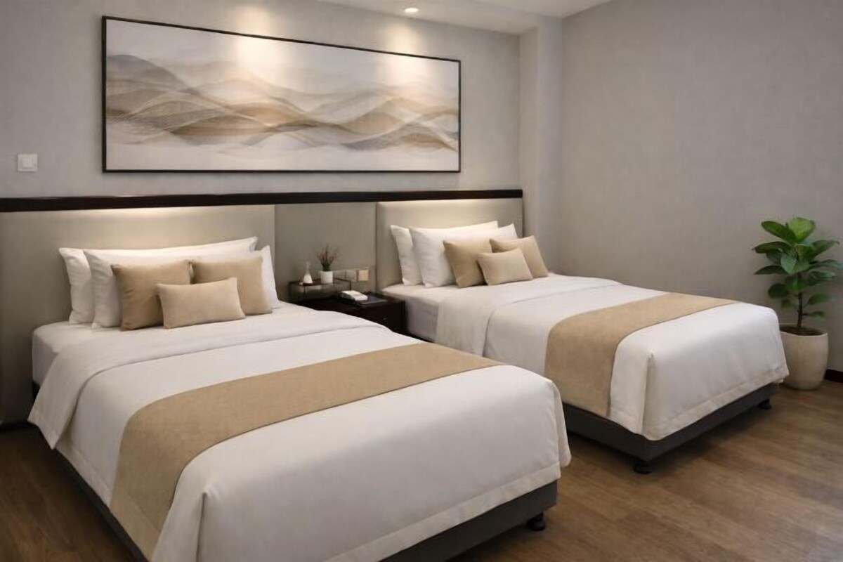 Habitación de hotel con dos camas, un cuadro abstracto grande en la pared, una mesita de noche y una planta en maceta.