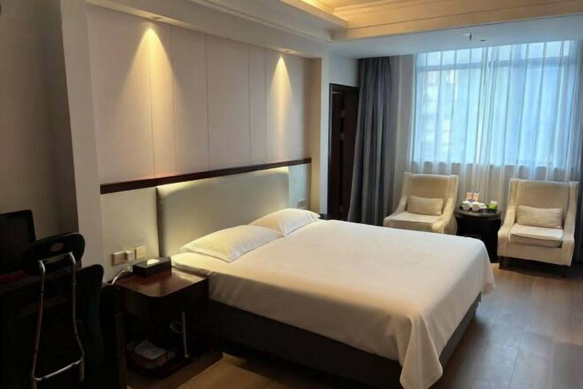 Ein Hotelzimmer mit einem großen Bett, zwei Sesseln, einem Schreibtisch und einem Fernseher.