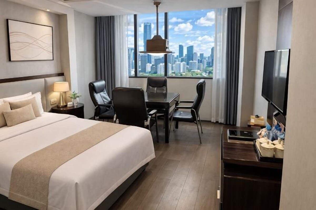 Habitación de hotel con cama, escritorio, sillas, televisión y vista a la ciudad.