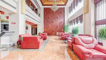 Vestíbulo de hotel con sofás rojos, un mostrador de recepción y una pared grande con un diseño geométrico.