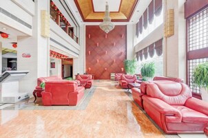 Vestíbulo de hotel con sofás rojos, un mostrador de recepción y una pared grande con un diseño geométrico.
