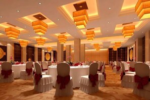Een balzaal met ronde tafels, witte stoelen met rode linten en sfeervol licht.
