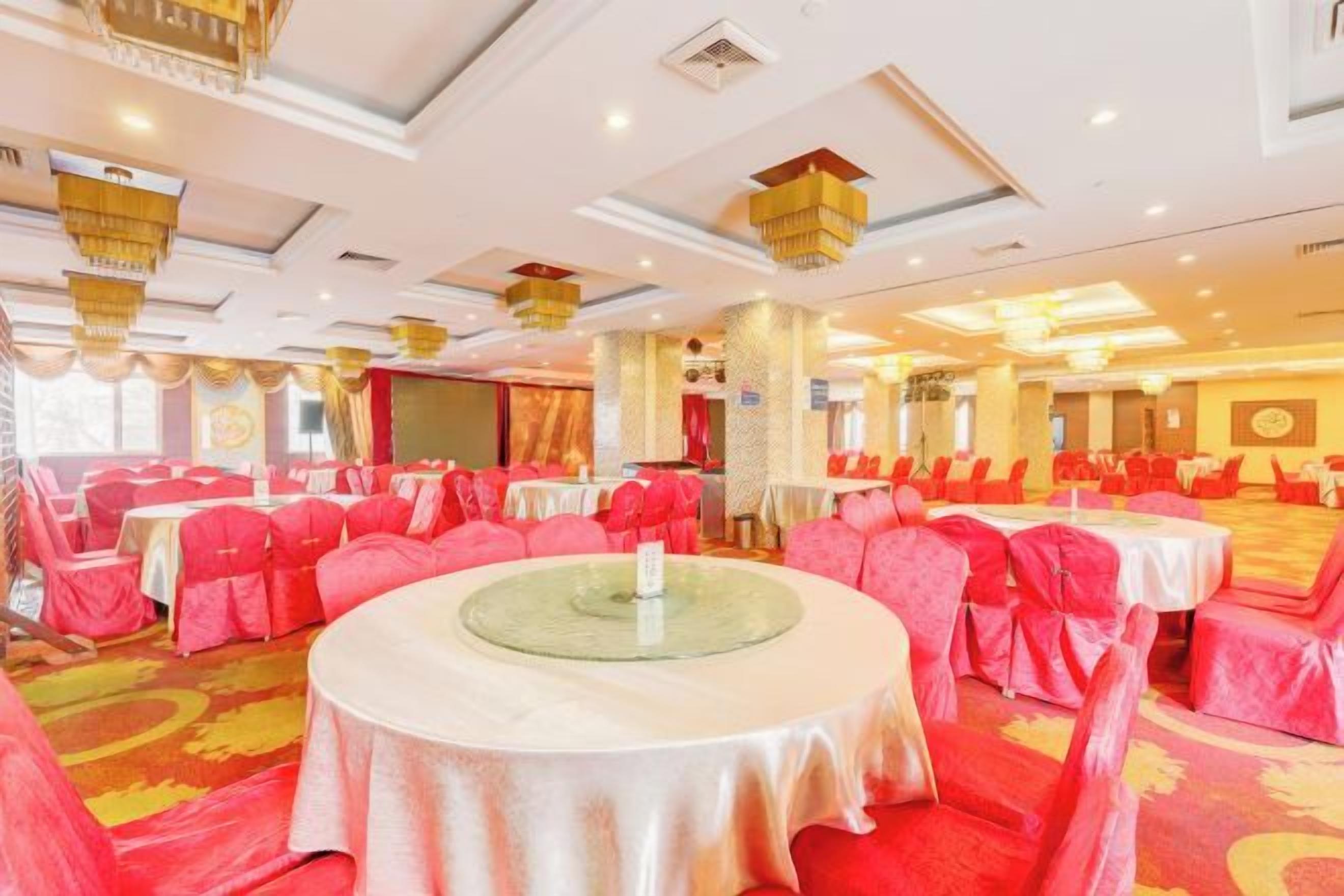 A banquet hall with round tables, red chairs, and a carpeted floor.