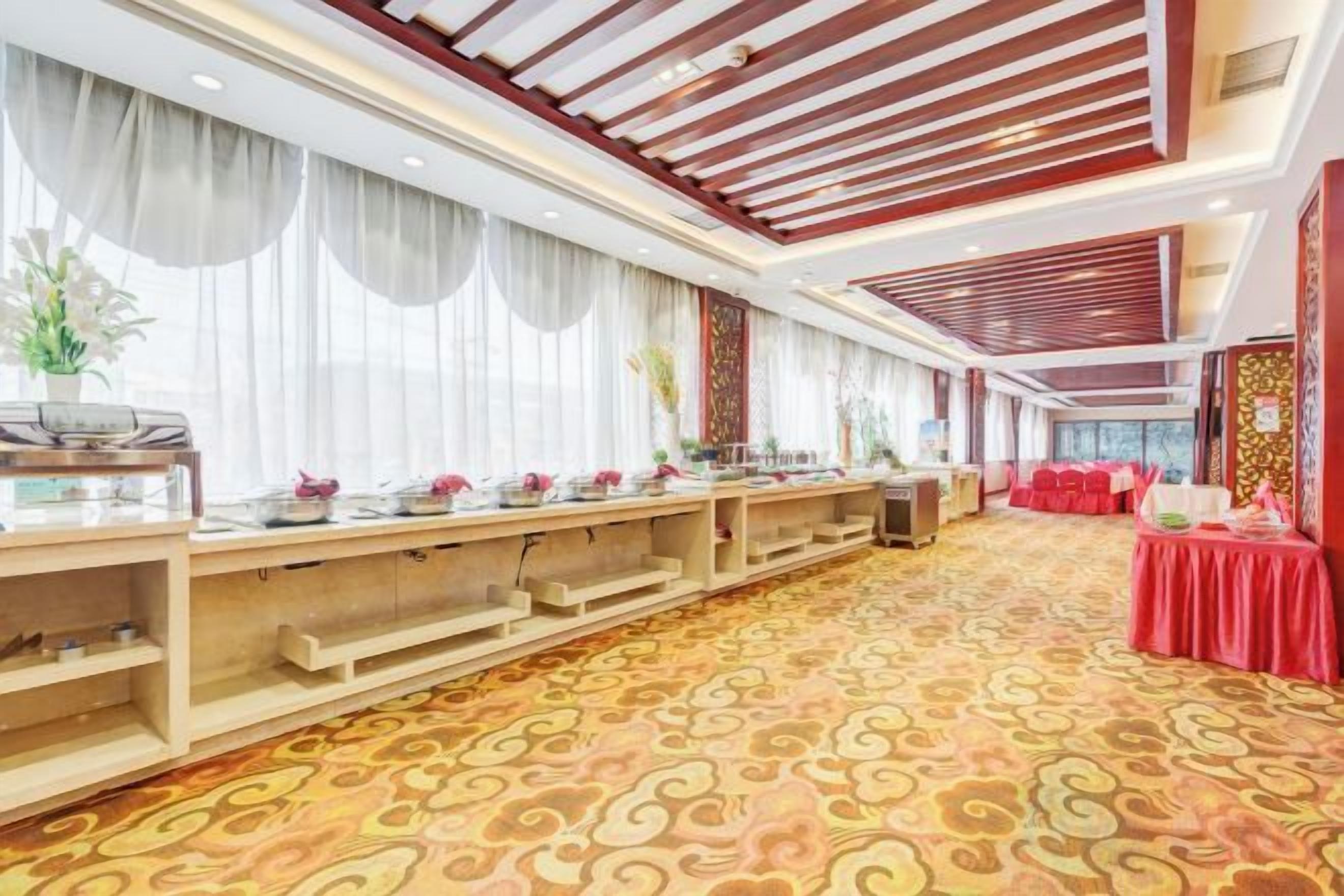 Un salón de banquetes con una larga mesa, manteles rojos y una alfombra estampada.