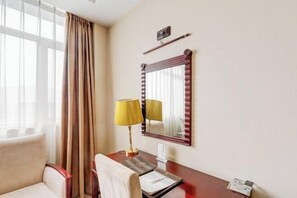 A hotel room with a desk, two chairs, a lamp, a mirror, and a window with curtains. - Zouping Hotel (Binzhou)