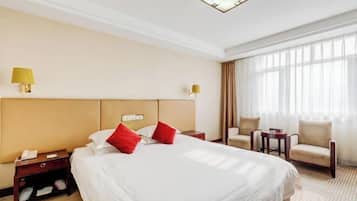 Una habitación de hotel con una cama grande, dos mesitas de noche, una silla, una pequeña mesa y un ventanal con cortinas.