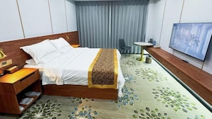 Een hotelkamer met een bed, nachtkastje, televisie en een eettafeltje met stoelen.