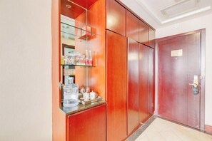 A hotel room with a wooden wardrobe, a small shelf with toiletries, and a red door. - Zouping Hotel (Binzhou)