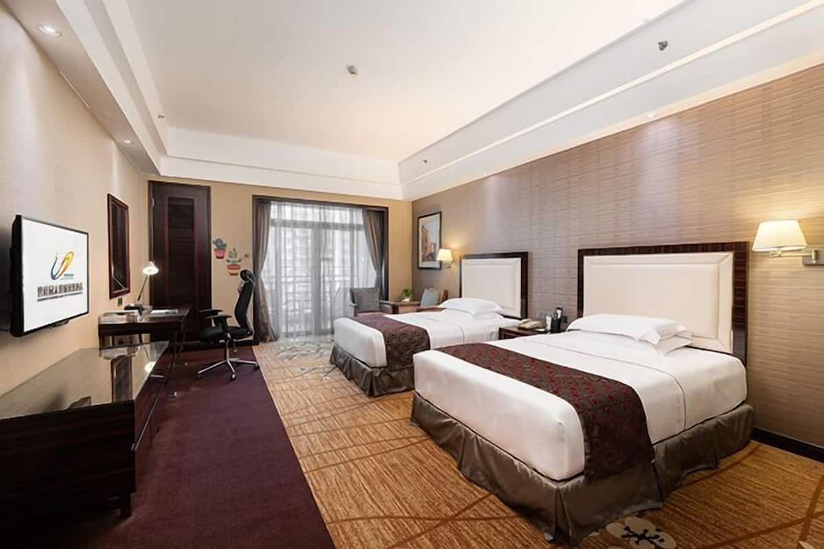 Ein Hotelzimmer mit zwei Betten, einem Schreibtisch, einem Sessel, einem Fernseher und einem großen Fenster mit Vorhängen.