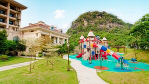 A playground with slides and climbing structures, a building with a red roof, and a pathway leading to the playground. - Country Garden Sun City Phoenix Hotel (Shaoguan)