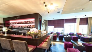 A bar area with a well-stocked liquor shelf, seating with cushioned chairs and ottomans, and a large window providing natural light. - TOP CityLine Hotel Platzhirsch Fulda (Fulda)