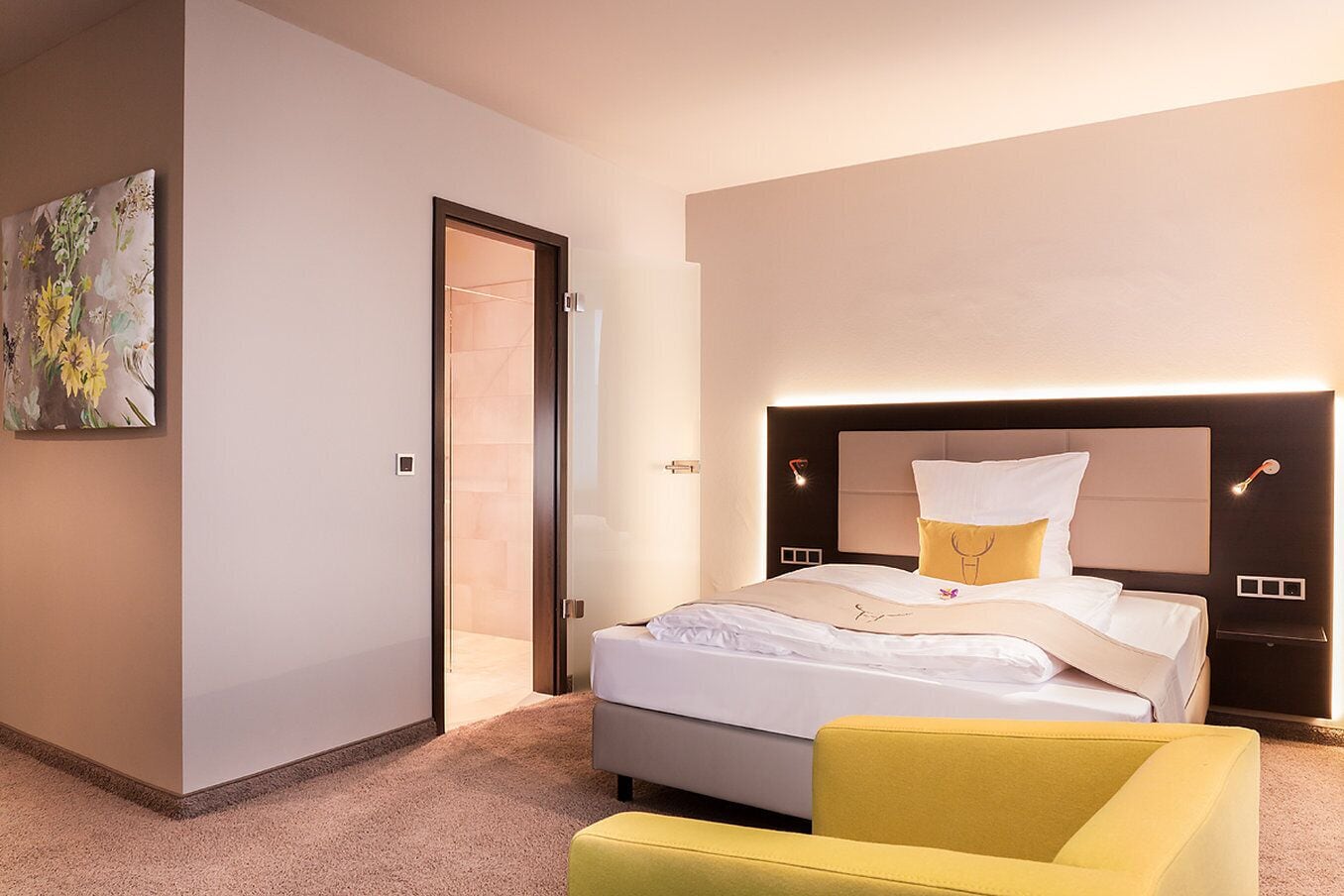 A modern hotel room with a large bed, a bedside table, a chair, and a painting on the wall.