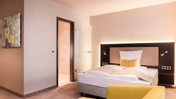 A modern hotel room with a large bed, a bedside table, a chair, and a painting on the wall.