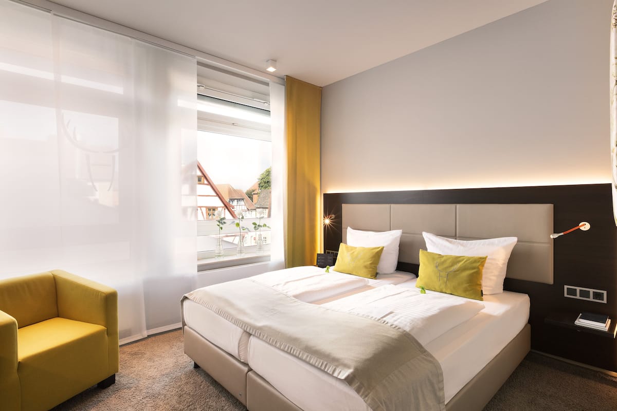 A modern hotel room with a large bed, a yellow armchair, and a view of the outside.