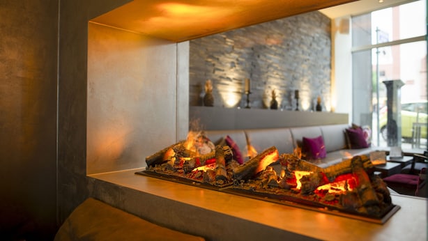 A modern interior with a fireplace, stone wall, and seating area. - TOP CityLine Hotel Platzhirsch Fulda (Fulda)