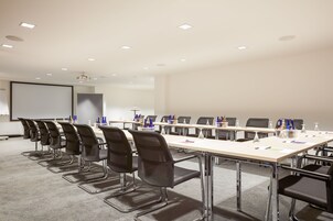 Un salón de conferencias con una larga mesa, varias sillas y una pantalla de proyector.