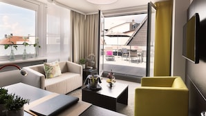 A modern living room with a sofa, yellow armchair, and a coffee table. There is a TV mounted on the wall and a window with curtains. - TOP CityLine Hotel Platzhirsch Fulda (Fulda)