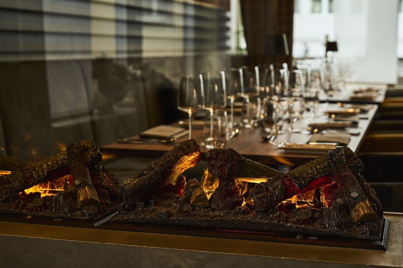 Una mesa de comedor con una estufa de leña en el centro, rodeada de sillas vacías y copas de vino.