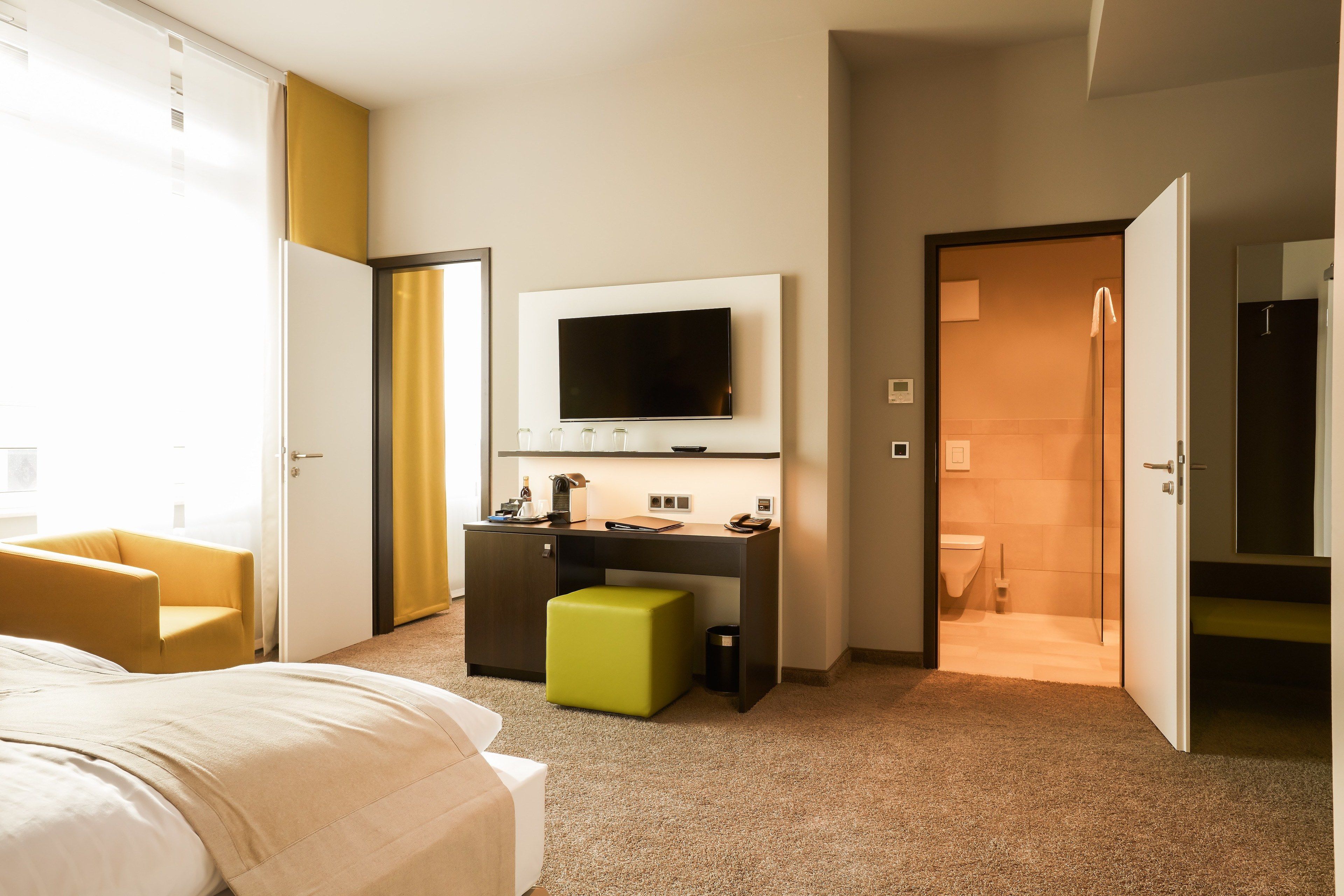 Habitación de hotel con cama, escritorio con televisor, una silla y baño visible a través de una puerta abierta.