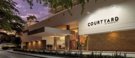 Una entrada de hotel moderna con el letrero 'Courtyard by Marriott', grandes ventanales y una fachada bien iluminada.