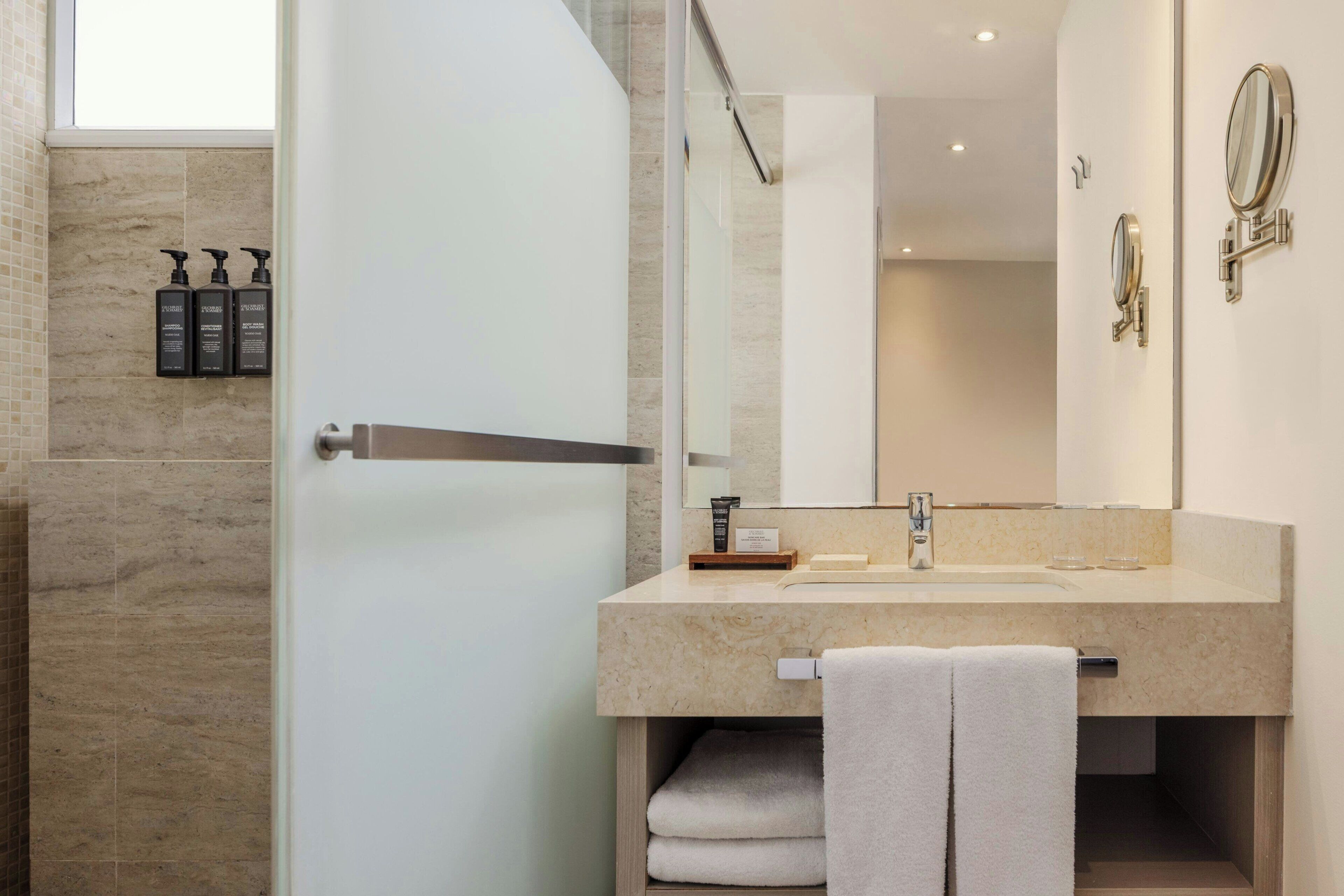 Une salle de bain moderne dotée d’une porte de douche en verre, d’un lavabo avec un meuble-vasque et d’un miroir agrémenté d’un miroir de coiffeuse.