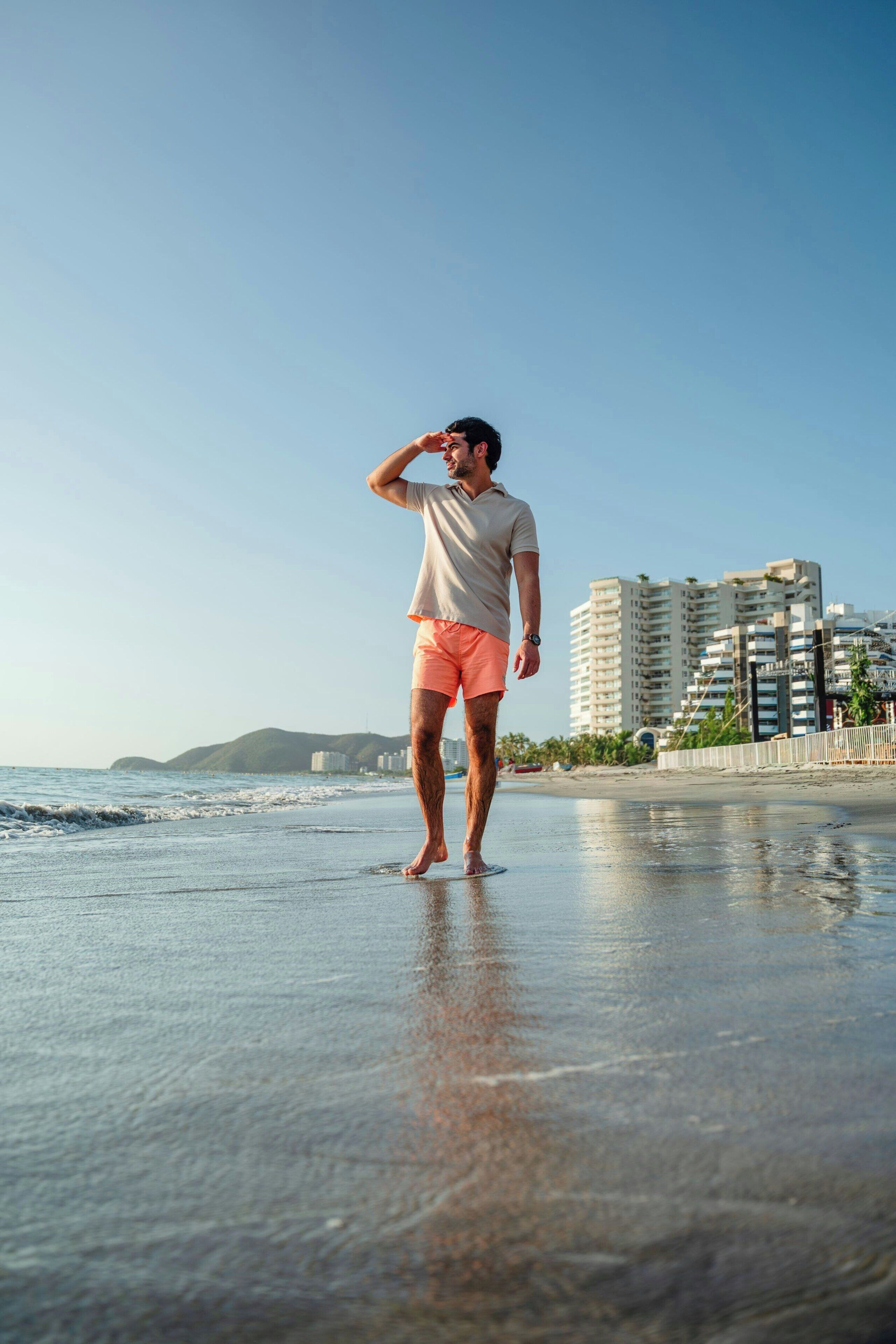 Una persona de pie en la playa, con un paisaje urbano al fondo.