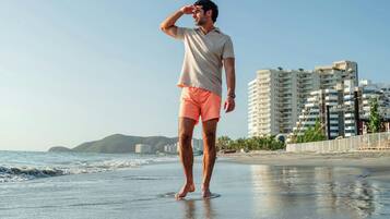 Una persona de pie en la playa, con un paisaje urbano al fondo.