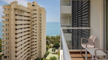 Un edificio de gran altura con balcones que dan a la costa, un balcón con una silla y una mesa, y vista al mar.