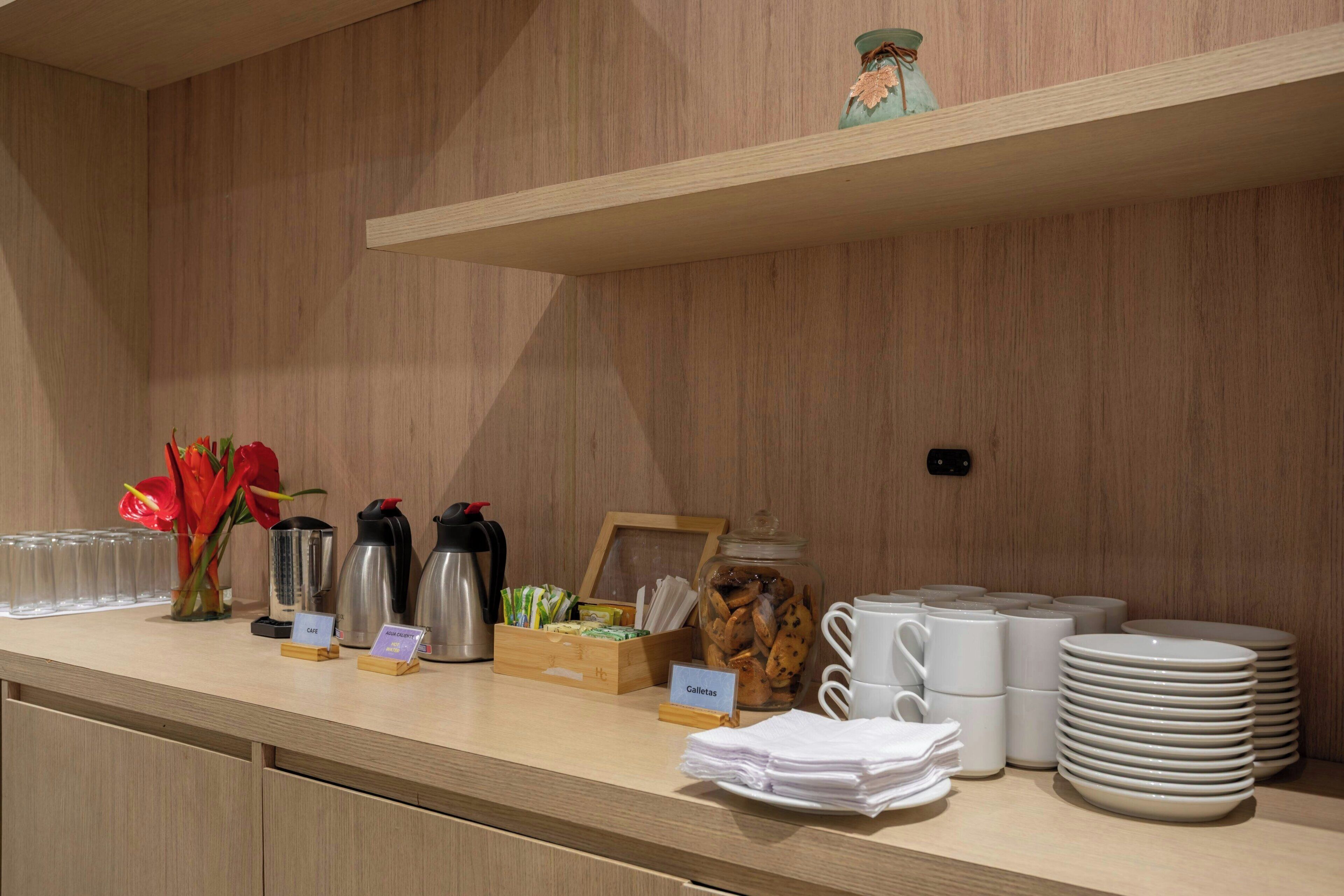 Angolo della colazione a buffet con macchine da caffè, un barattolo di biscotti e pile di piatti e ciotole.