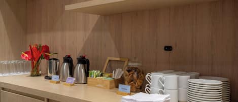 A breakfast buffet area with coffee makers, a jar of cookies, and stacks of plates and bowls.