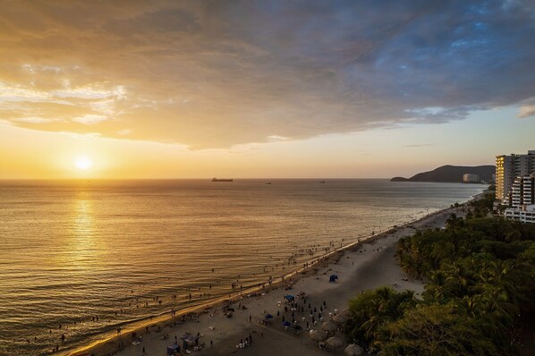Una playa con un atardecer, mar en calma y un barco a lo lejos.