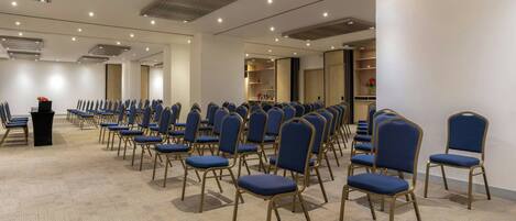 A conference room with rows of blue chairs and a podium.