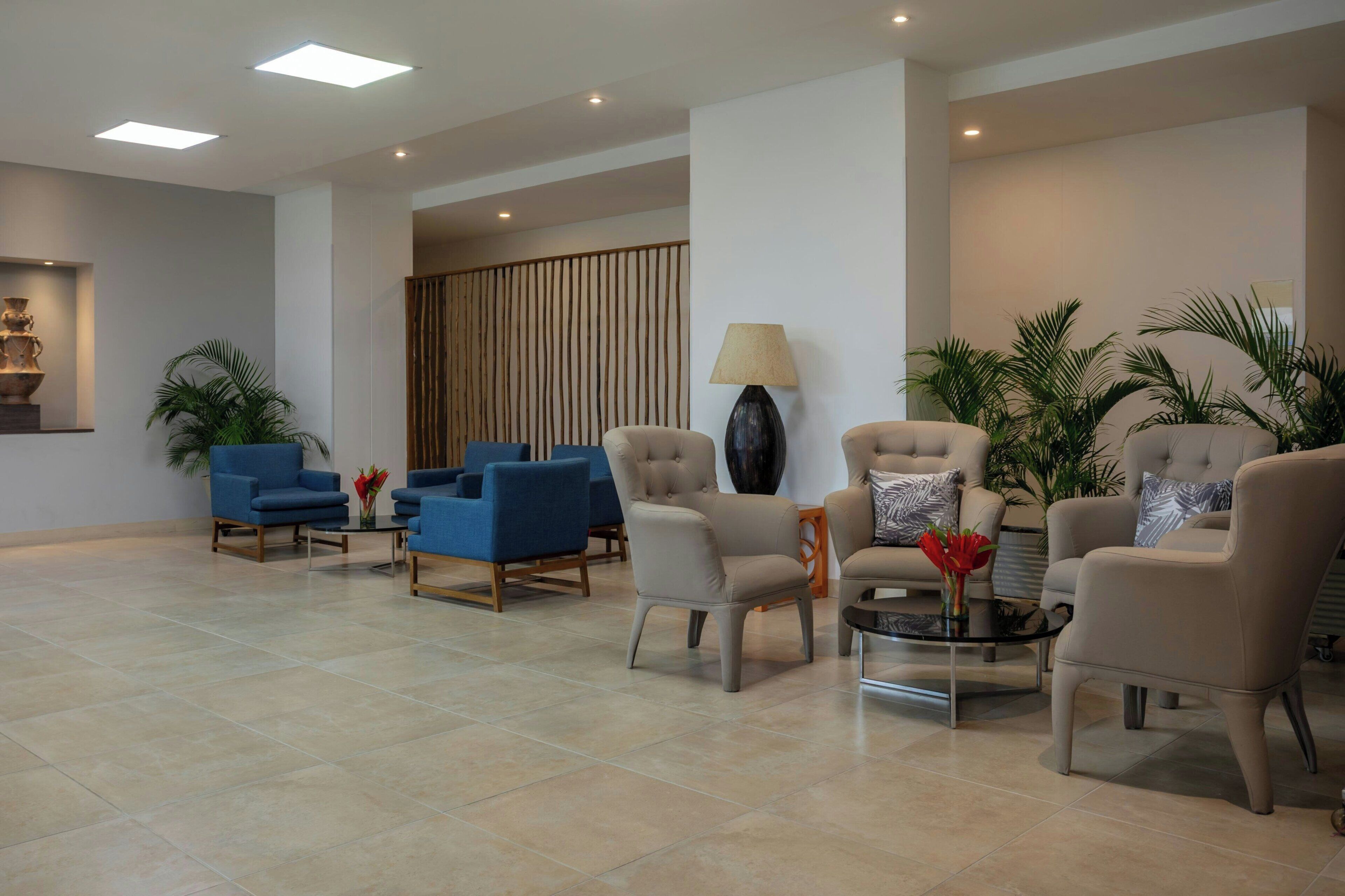 Um hall amplo com assentos modernos, uma luminária grande e plantas decorativas.