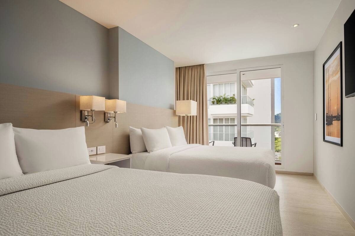 A hotel room with two beds, a balcony with a view, and a mounted TV.