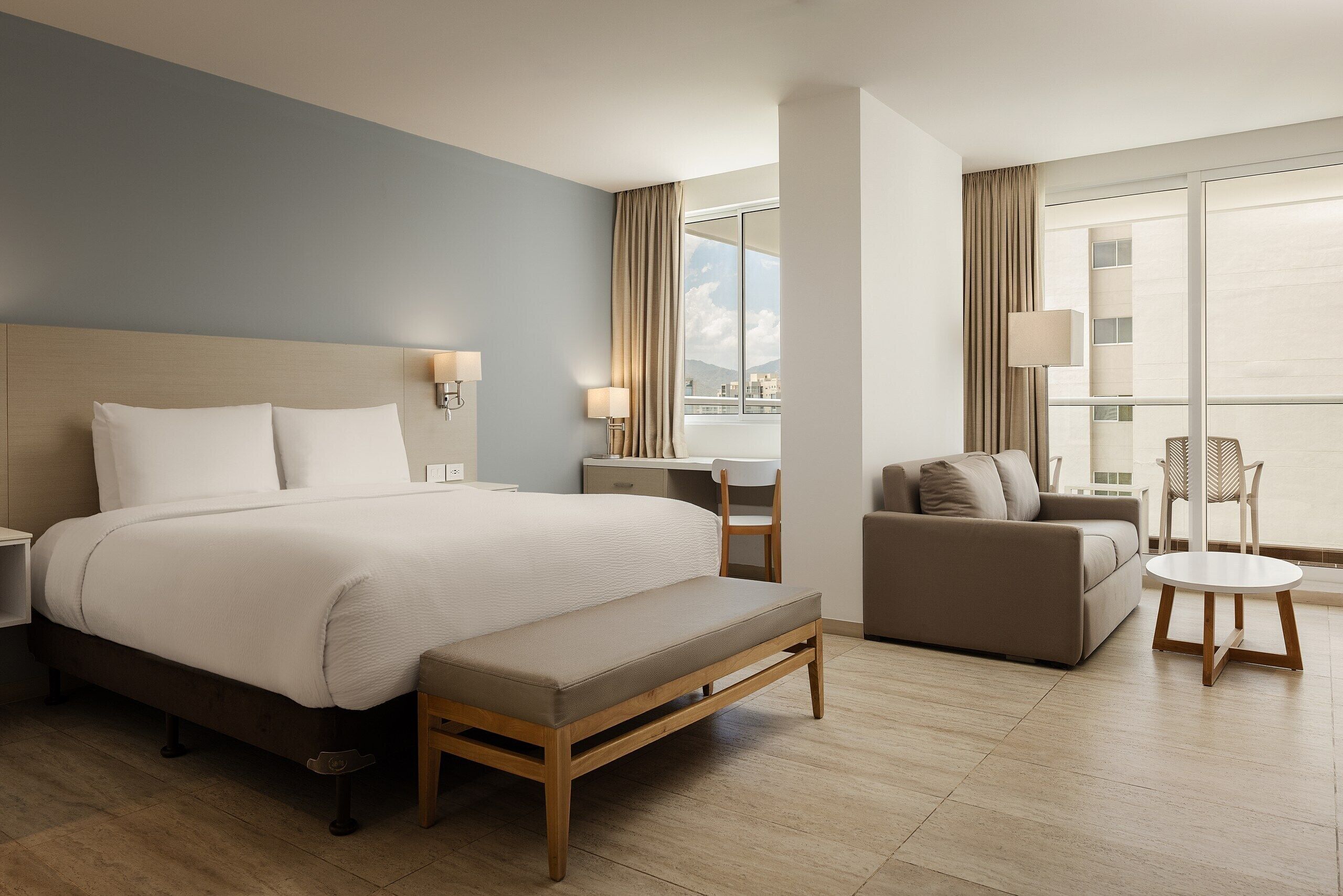 Ein Hotelzimmer mit einem großen Bett, einem Schreibtisch, einer Couch und einem Balkon mit Blick.