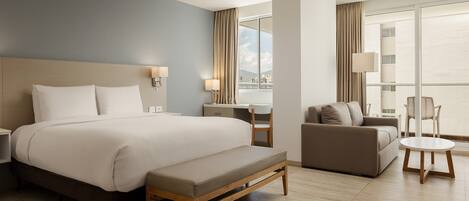 A hotel room with a large bed, a desk, a sofa, and a balcony with a view.