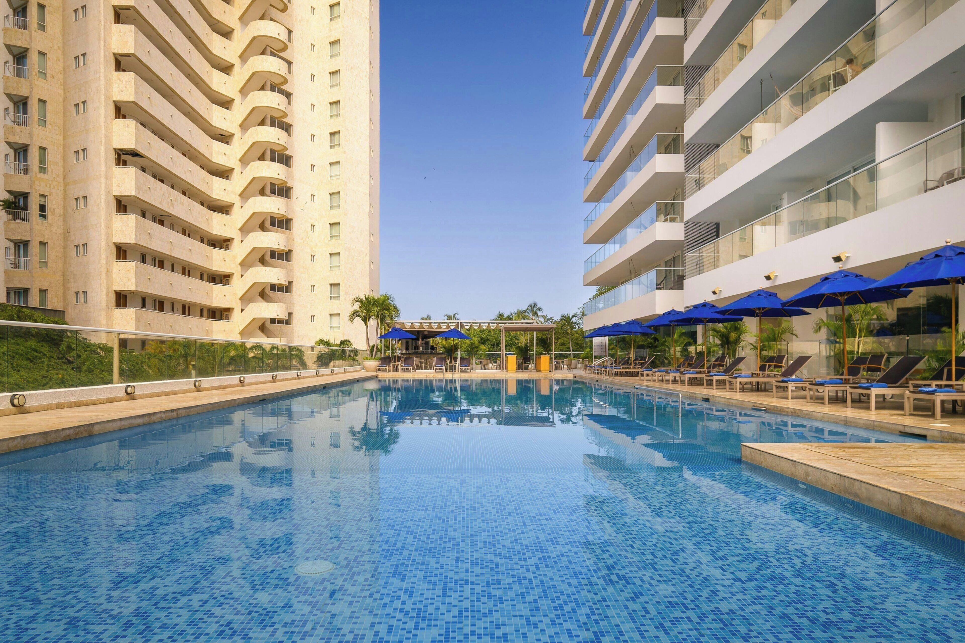 A swimming pool with lounge chairs and umbrellas, surrounded by high-rise buildings.