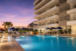 Un hotel moderno con piscina, sillas de descanso y sombrillas.