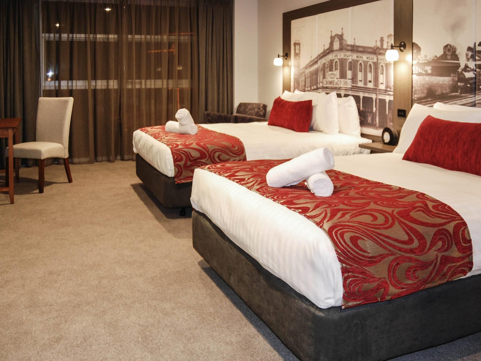 A hotel room with two beds, a chair, a desk, and a large framed picture on the wall.