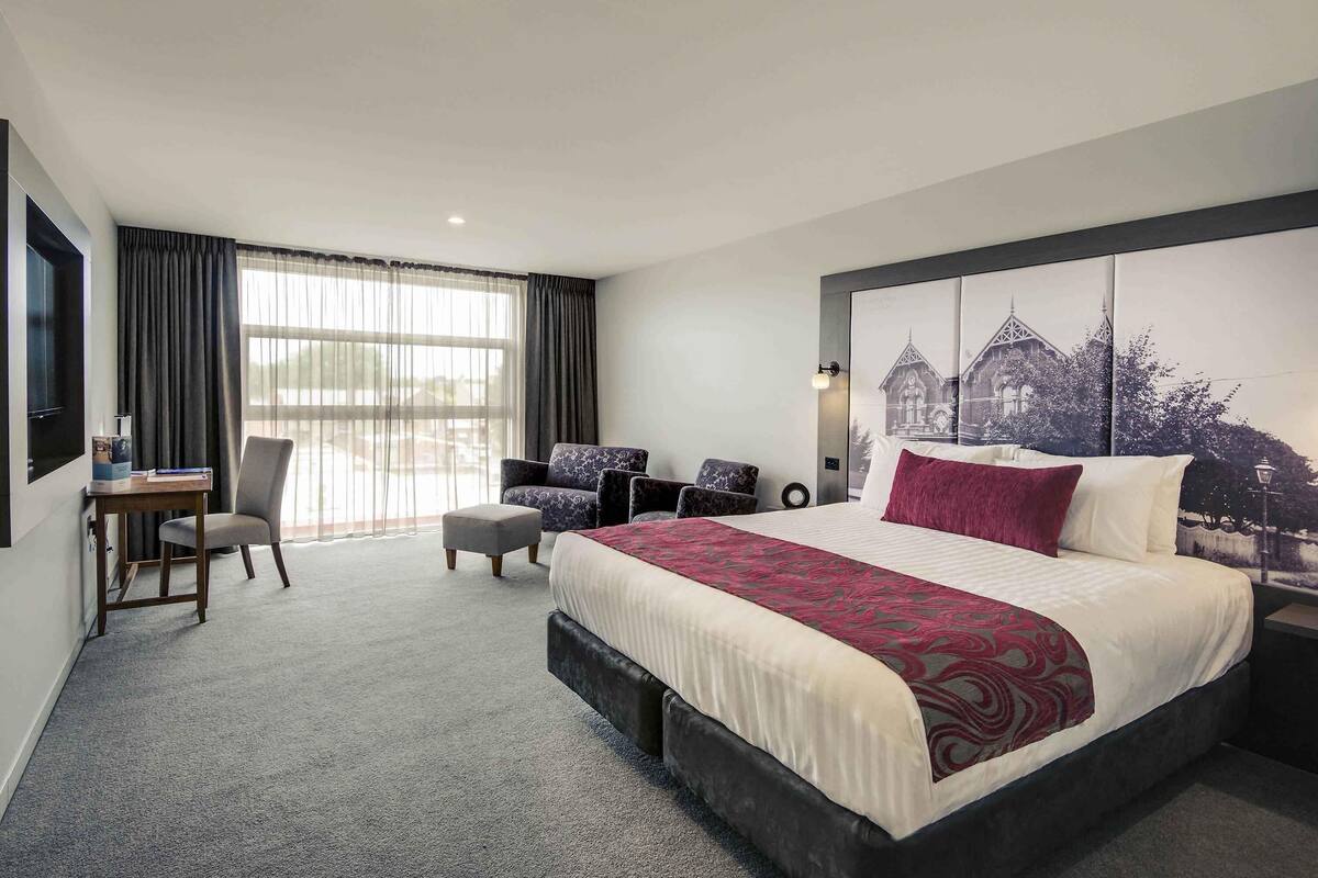 Habitación de hotel con una cama grande, un escritorio, una silla y vista a un edificio por la ventana.